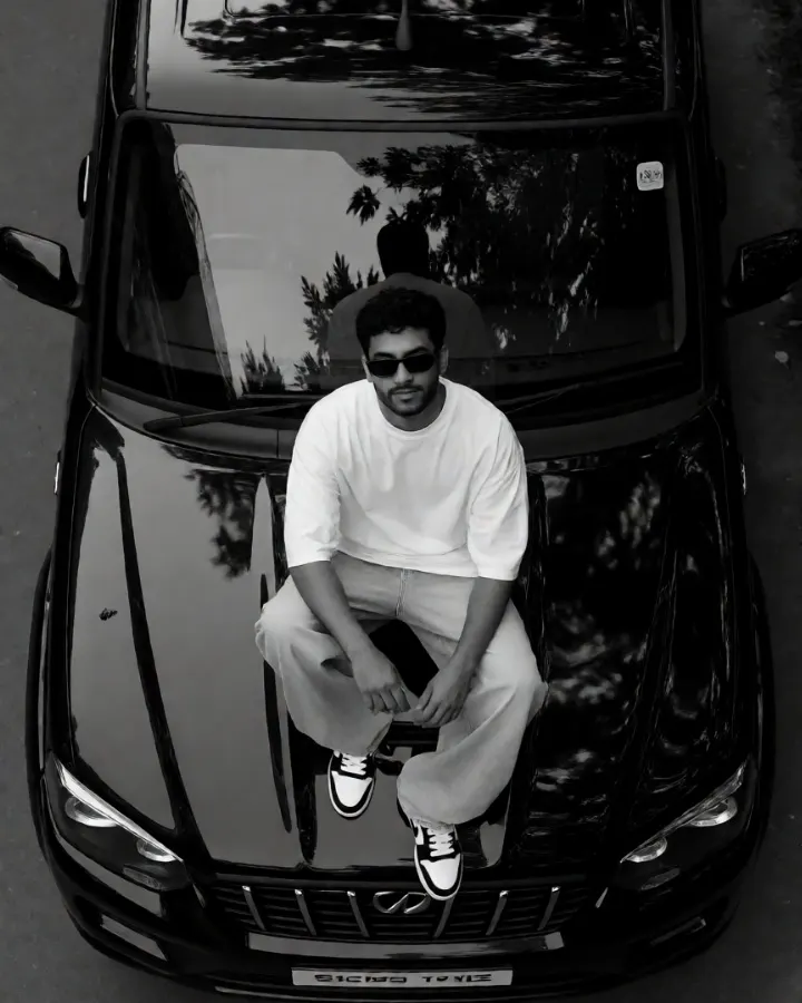 AI-generated image: A confident young Indian male sitting on the bonnet of a black Mahindra Scorpio SUV with natural outdoor lighting.